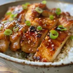 Pollo Teriyaki jugoso presentado en un plato con un fondo desenfocado.